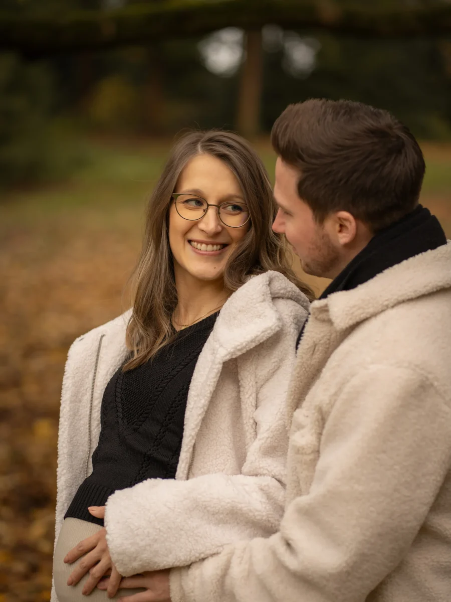 Werdende Eltern Arm in Arm, Hände auf dem Babybauch – Babybauch-Shooting im Herbst
