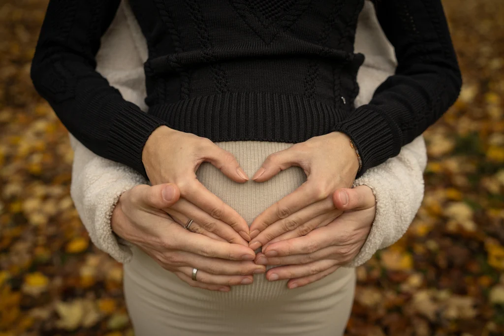 Hände formen ein Herz auf dem Babybauch – Babybauch-Shooting im Herbst