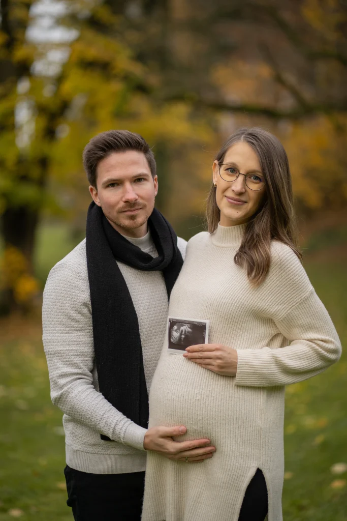 Werdende Eltern mit Ultraschallbild vor herbstlichen Bäumen – Babybauch-Shooting