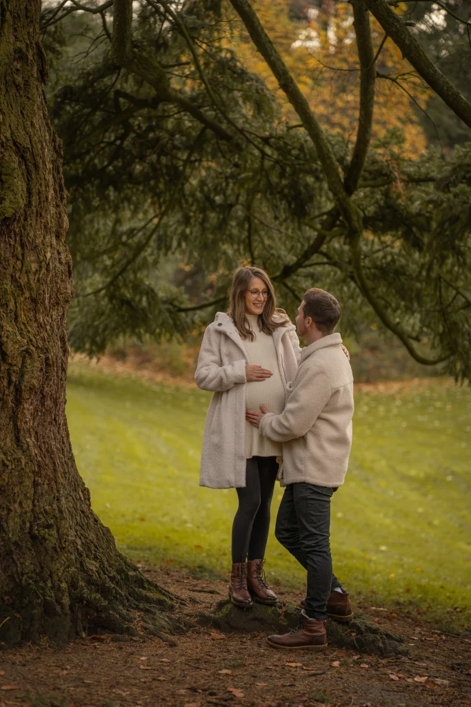 Paar mit Babybauch unter einem großen Baum im Herbst – Mosipictures