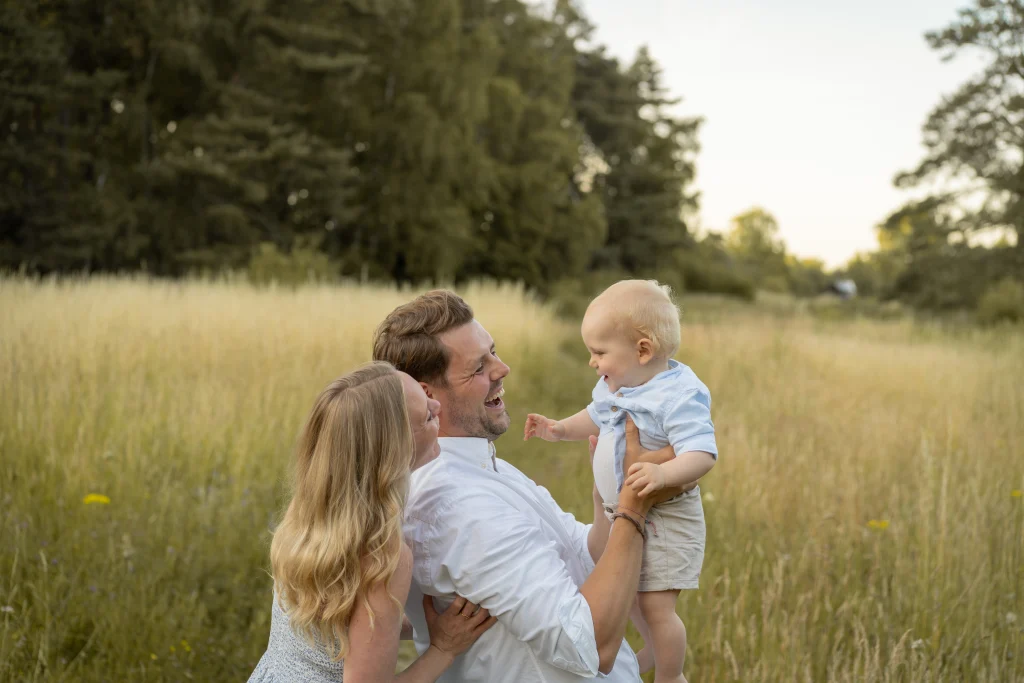 Eltern halten ihr lachendes Kind im hohen Gras – Familienshooting im Sonnenuntergang