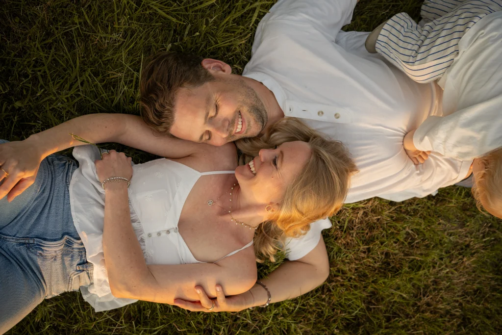 Eltern liegen eng aneinander im Gras – Familienshooting im Sonnenuntergang